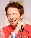 A man with red hair, smiling slightly and sitting behind a microphone.