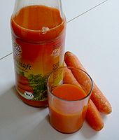 Une bouteille de jus, un verre de jus et des carottes