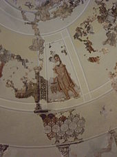 La photographie couleur représente une coupole peinte dans un mausolée. Les restes abîmés des peintures rupestres laissent voir un jeune homme portant trois grappes de raisin.
