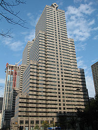 A high, stair-shaped building against a blue sky, with other, similar buildings around it.