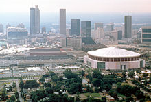 Vue aérienne de la ville d'Atlanta aux États-Unis. De la végétation et des habitations sont visibles au premier plan. Le Georgia Dome, stade couvert destiné aux matchs de football américain, est situé au second plan. On aperçoit des immeubles et des buildings en arrière-plan.