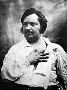 Photographie noir et blanc, Honoré de Balzac, d'âge mûr, cheveux et moustache noirs, vêtu d'une chemise blanche, pose en buste, la main à plat sur le cœur.