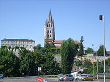 Photographie d'une basilique au clocher de style gothique sur un promontoire avec au premier plan un grand carrefour routier