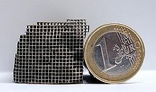 Photographie d'une pièce métallique formant un labyrinthe tridimensionnel. Une pièce de monnaie est appuyée contre celle-ci.