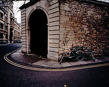 Une grande arche de pierre ouvrant à l'intersection de deux rues, avec deux vélos appuyé contre un mur