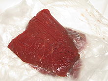 Morceau de viande de couleur rouge assez foncée et de forme carrée.