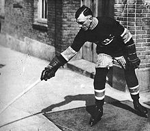 Photo noir et blanc de Joe Hall en tenue de hockeyeur à l'extérieur d'un bâtiment.