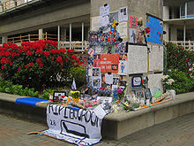Photo de messages et photos à la mémoire de Bourdon sur un pilier près d'un massif de fleurs.