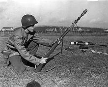 Photographie d'un soldat tenant entre ses mains un fusil armé d'une grenade.