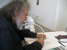 La photo montre un homme barbu assis de profil.