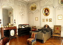 salle couverte de boiseries blanches, avec contre les murs, une cheminée, une vitrine et un lit surmonté d'un portrait. Trois fauteuils sont disposés au centre de la pièce