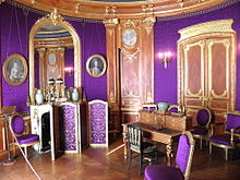 salle ronde aux murs couverts de violet et de boiseries dorées avec miroirs et portraits au pastel. La salle comprend un secrétaire au centre, un paravent et des chaises tapissés de violet