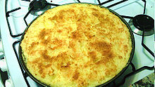 Plat rond de pastel de papa posé sur une palque de cuisson au gaz et montrant la couche de fromage râpé gratinée de couleur jaune orangé