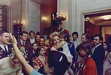 Pat Nixon tenant une enfant dans ses bras, au milieu d'autres et de visiteurs à la Maison-Blanche.
