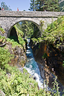 Un pont de pierre enjambe une rivière fougueuse dans un cadre naturel.