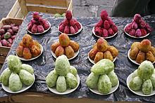 Des figues de barbarie pelées, de couleur verte, jaune ou rouge, empilées dans des coupelles sur une étale de marché