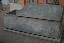 sarcophage en pierre couvercle à demi-soulevé. Divers motifs gravés : deux lions, un paon, un symbole christique, une fontaine