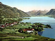 L'illustraton est une photographie ancienne colorisée. Elle montre un village accolé au lac d'Annecy. Tous les coteaux au premier et deuxième plan sont couverts de vigne. En arrière plan, les pentes fortes sont boisées.