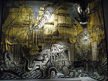Fresque murale à dominantes dorée et argentée représentant des navires à voile et à vapeur, et des créatures marines mythiques.