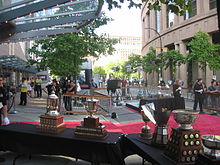 Photo couleur de plusieurs trophées exposés sur des tables dans une rue arborée.