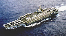 Vue aérienne du porte-avions ; les marins sont disposés de manière à écrire “Big Stick” sur le pont d'envol.