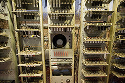 Plan rapproché sur trois grands casiers contenant des circuits électroniques, avec un tube cathodique au milieu du casier central. Sous le CRT, il y a un tableau de contrôle contenant quatre rangées de huit interrupteurs.