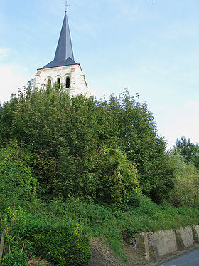 Le clocher de pierre, d'un blanc éclatant dû à une restauration récente, surgit de la butte boisée surplombant une partie du village.
