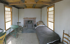 L'intérieur de la cabane de Thoreau. Au fond et au centre : une cheminée de briques rouges à côté de laquelle est une caisse de bois de chauffe et à droite et à gauche : deux fenêtres. À droite, un lit fait ; à gauche, une chaise et une petite table ronde. On aperçoit sur le côté gauche, au premier plan, une partie d'un secrétaire pour écrire.