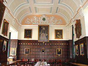 Un hall lambrissé de bois, avec un grand portrait d'Elizabeth I au milieu du mur du fond, d'autres  portraits sur les murs ; un plafond de plâtre blanc à décor bleu clair