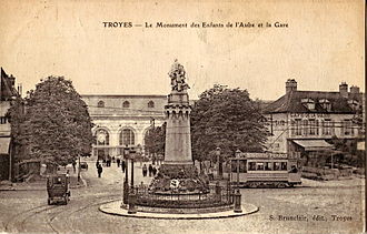 Carte postale ancienne montrant une motrice du Tramway de Troyes derrière le Monument des Enfants de l'Aube, et, en arrière plan, la Gare