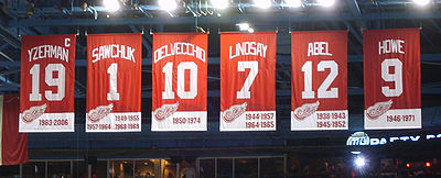 Photo des bannières des maillots retirés des Red Wings avec leur nom, leur numéro et la ou les périodes où ils ont joué avec l'équipe. De gauche à droite, Yzerman dont la bannière porte en plus le C de capitaine, Sawchuk, Delvecchio, Lindsay, Abel et Howe.